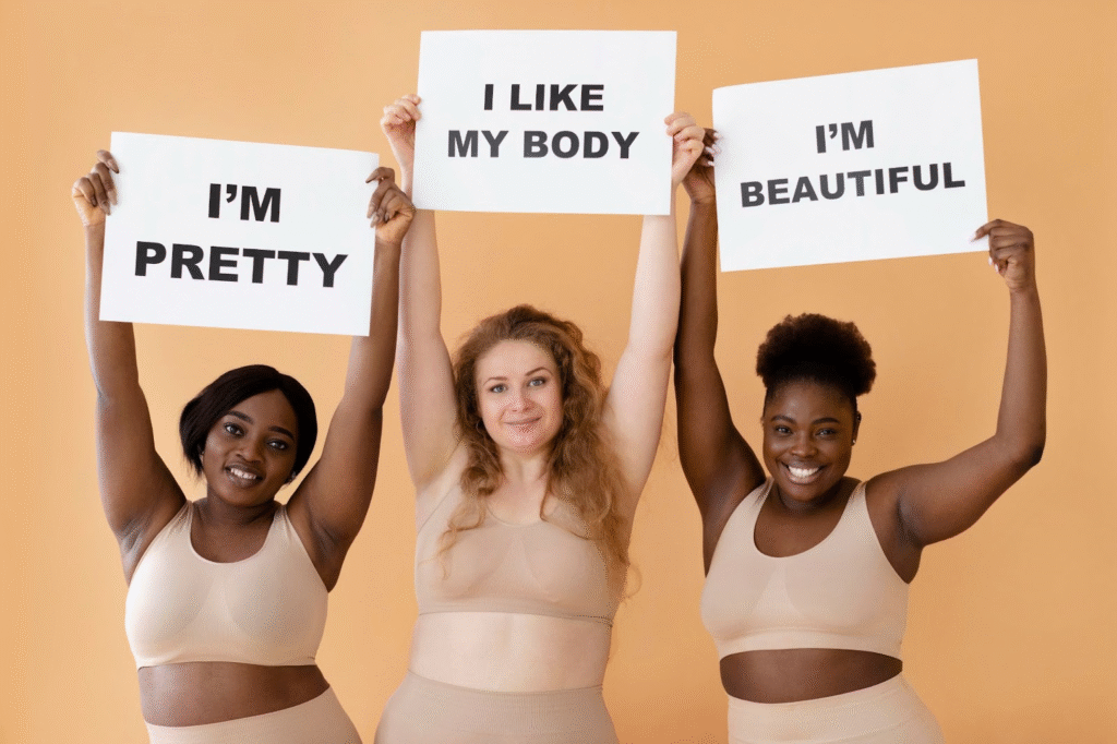 Three women in beige outfits holding body positivity signs with smiles.