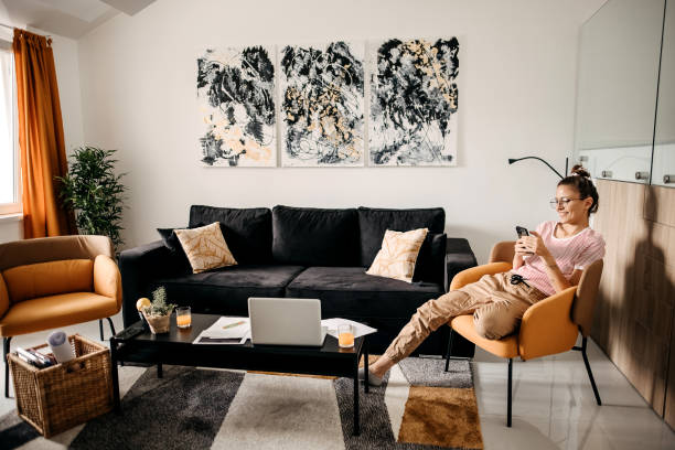 Cozy living room with stylish furniture where a person sits comfortably, browsing on a phone beside a coffee table.